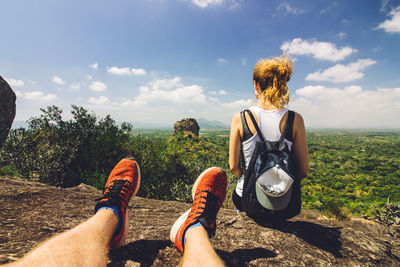 Low section of men sitting on landscape against sky