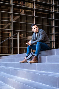 Young casual wearing man sitting at the entrance of an office building