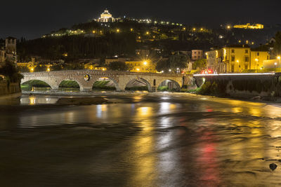 Illuminated bridge over river by buildings in city at night