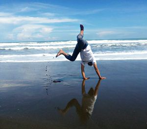 Full length of playful man practicing cartwheel on shore at beach