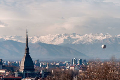 Old church in city by snow covered mountains against cloudy sky