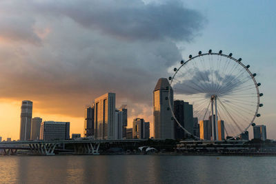 Bridge over river by buildings against sky during sunset