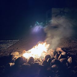 Bonfire by rocks on beach against sky at night