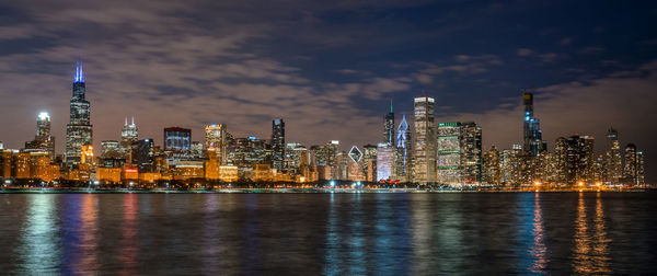 Illuminated city by buildings against sky at night