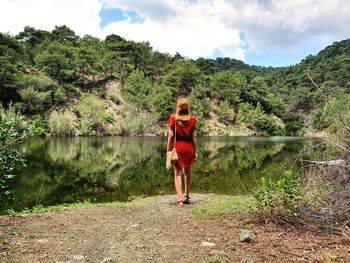 Rear view of woman standing by lake against sky /  woman in red dress / green landscape