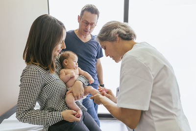 Female doctor examining baby boy with parents at hospital