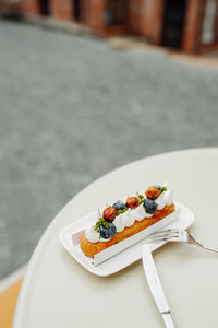 Eclair with white cream, fresh blueberries and caramel in  plate with fork, spoon. outdoor cafe.