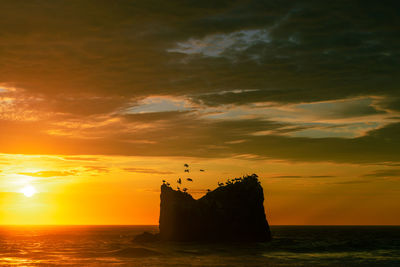 Silhouette rocks by sea against sky during sunset