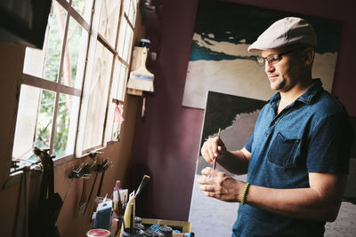Mid adult male cuban artist mixing paint with brush in his workshop