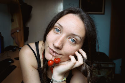 Close-up portrait of woman holding cherries in mouth at home
