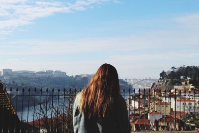 Rear view of woman looking at cityscape against sky