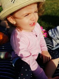 High angle view of cute baby girl wearing hat sitting in park during sunny day