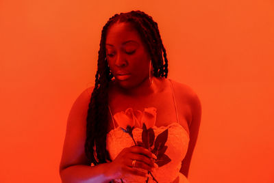 Braided black woman looking away against orange background