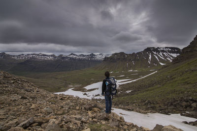 Rear view of hiker standing by mountains against cloudy sky