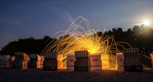 Illuminated wire wool amidst hooded chairs at beach during night