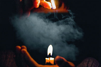 Close-up of hands holding lit candles against black background