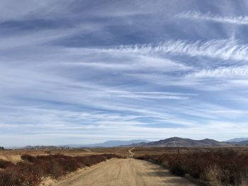 Dirt road amidst landscape against sky