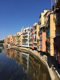 Buildings by river against clear blue sky