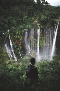 High angle view of man standing on mountain against waterfall at forest