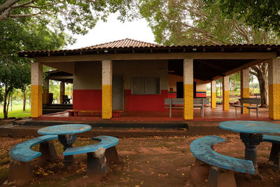 Empty chairs and tables by house against sky