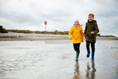 Full length portrait of girl walking with brother at beach