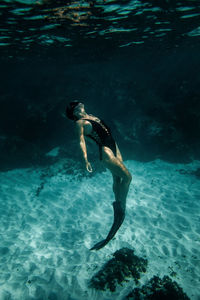 Side view of slim female in swimsuit and flippers swimming underwater in turquoise sea