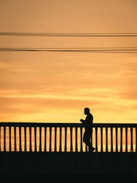 Silhouette man standing on footbridge over sea against sky during sunset