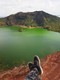 Low section of person on lake by mountain against sky