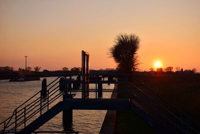 Silhouette bridge over river against sky during sunset