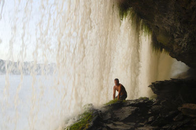 Man kneeling on rock formation by waterfall