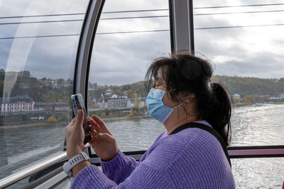 Woman using mobile phone by window against sky