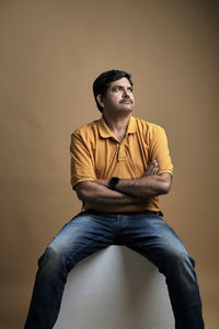Side view of young man sitting on chair against blue background