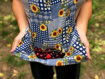 Midsection of woman holding berry fruits in top while standing at farm