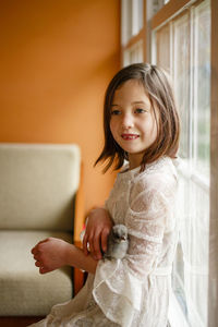 A little girl with missing teeth sits with baby chick nestled in arms