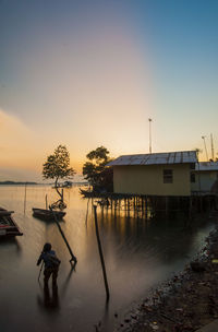 Rear view of photographer photograph in river by house during sunset