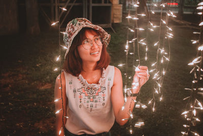 Smiling young woman wearing eyeglasses looking illuminated lights at night