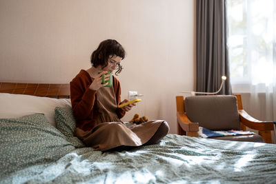 Young woman using phone while lying on bed at home