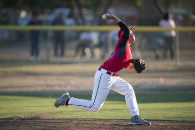 Teen baseball player pitching in red uniform in wind up on the mound