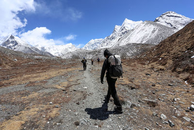 Rear view of people walking on landscape with snowcapped mountains in background