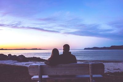 Silhouette people sitting on beach against sky during sunset