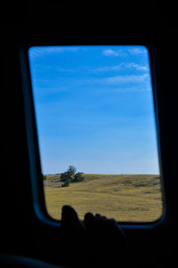 Close-up of hand against sky seen through window
