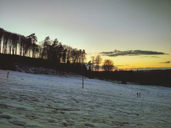 Silhouette trees on snow covered land against sky during sunset