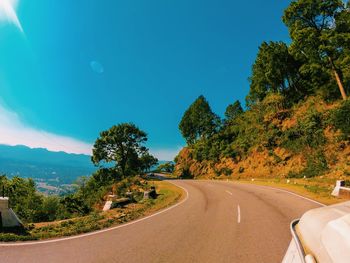 Road by trees against blue sky