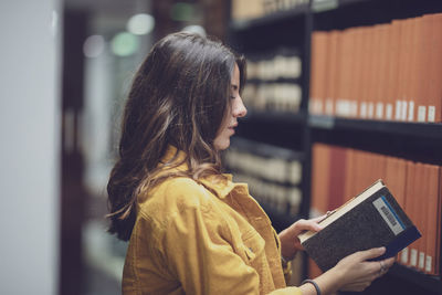 Side view of young woman holding book at library