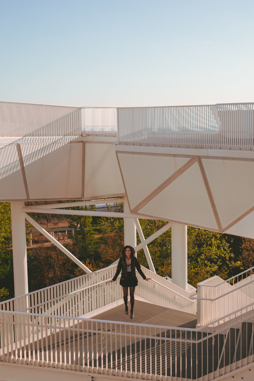 REAR VIEW OF WOMAN STANDING ON FOOTBRIDGE