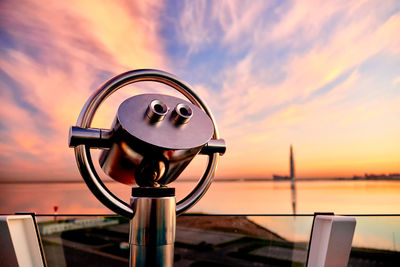 Close-up of coin-operated binoculars against sea during sunset