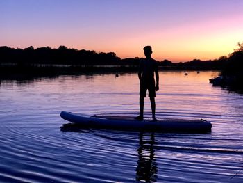 Boy standing over boat on lake against sky during sunset