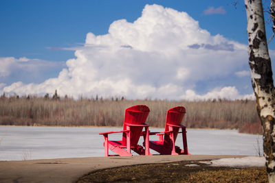 Red chair by lake against sky