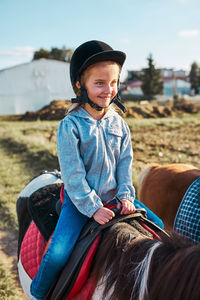 Little smiling girl learning horseback riding. 5-6 years old equestrian in helmet