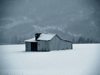 House on snow covered land against trees and houses during winter